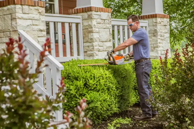 man using a Stihl hedge trimmer, one of the essential pieces of outdoor power equipment for homeowners, to maintain his landscaping